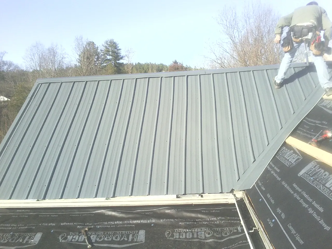 Crew installing dark green standing seam panels over synthetic underlayment in Lakebay