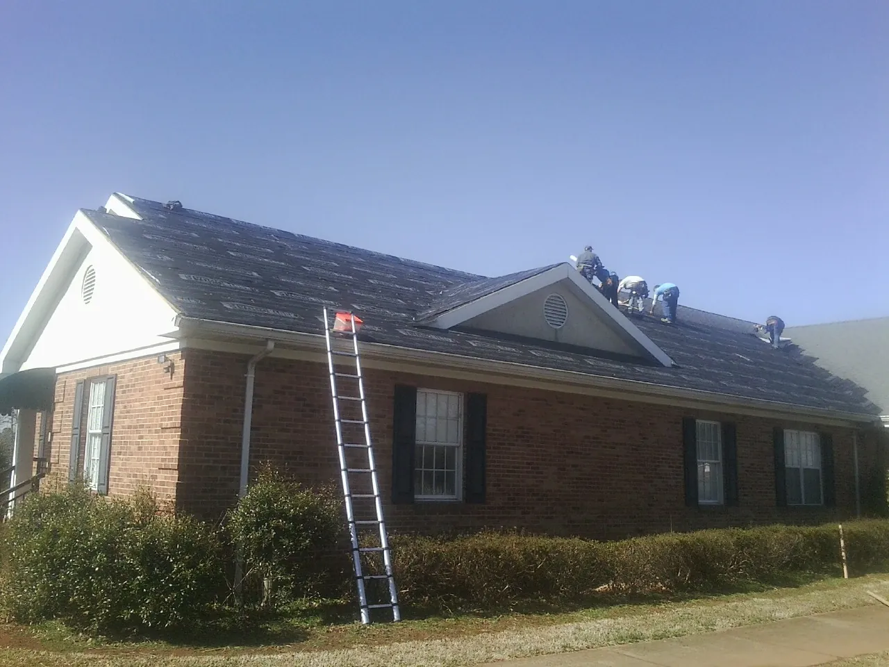 Crew tearing shingles off a brick ranch roof with a ladder set — Metal Roof Repair work by our crew in Lakebay