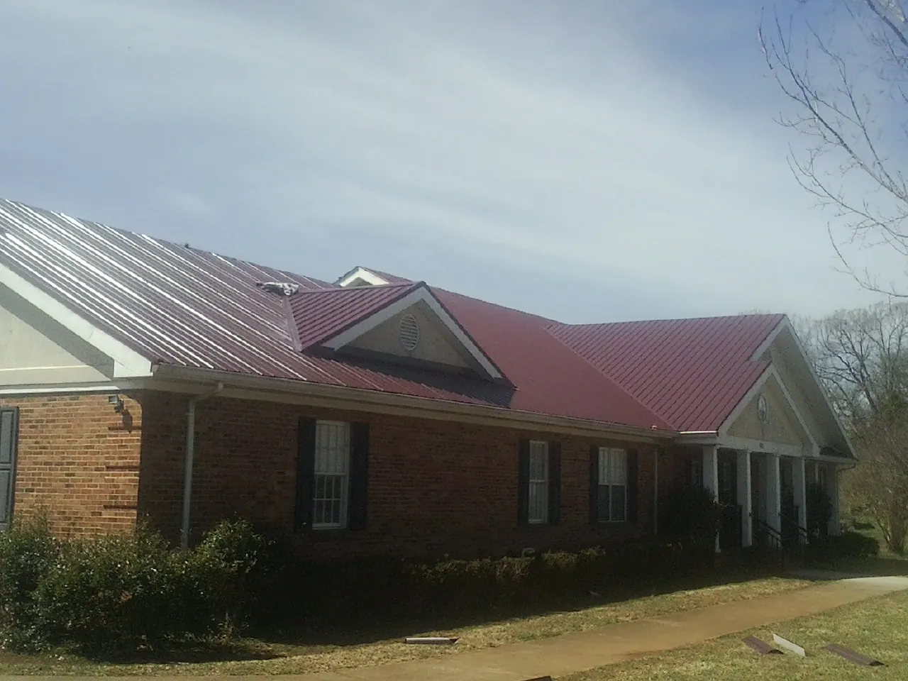 Red metal roof with gabled entries on a long brick building, from a Hail Damage Roof Repair job in Lakebay