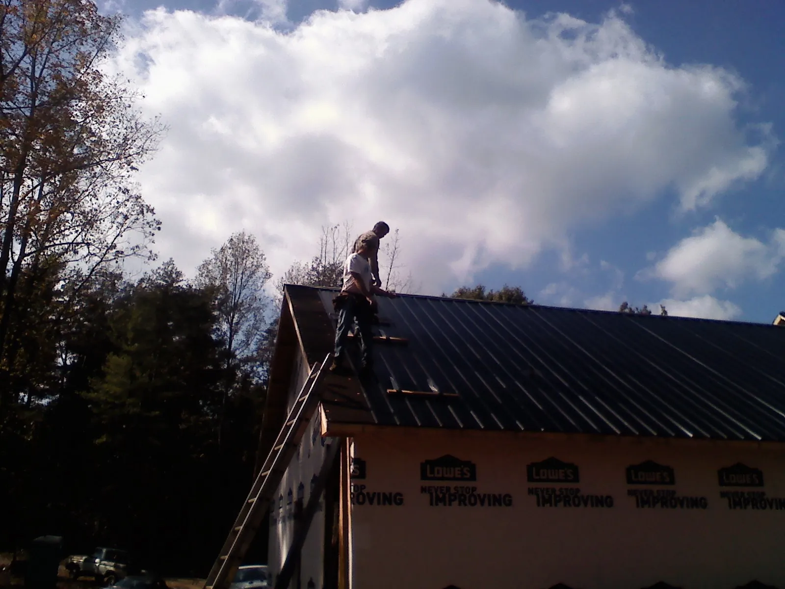 Roofer fastening dark metal panels high against a cloudy sky, from a Roof Inspection job in Lakebay