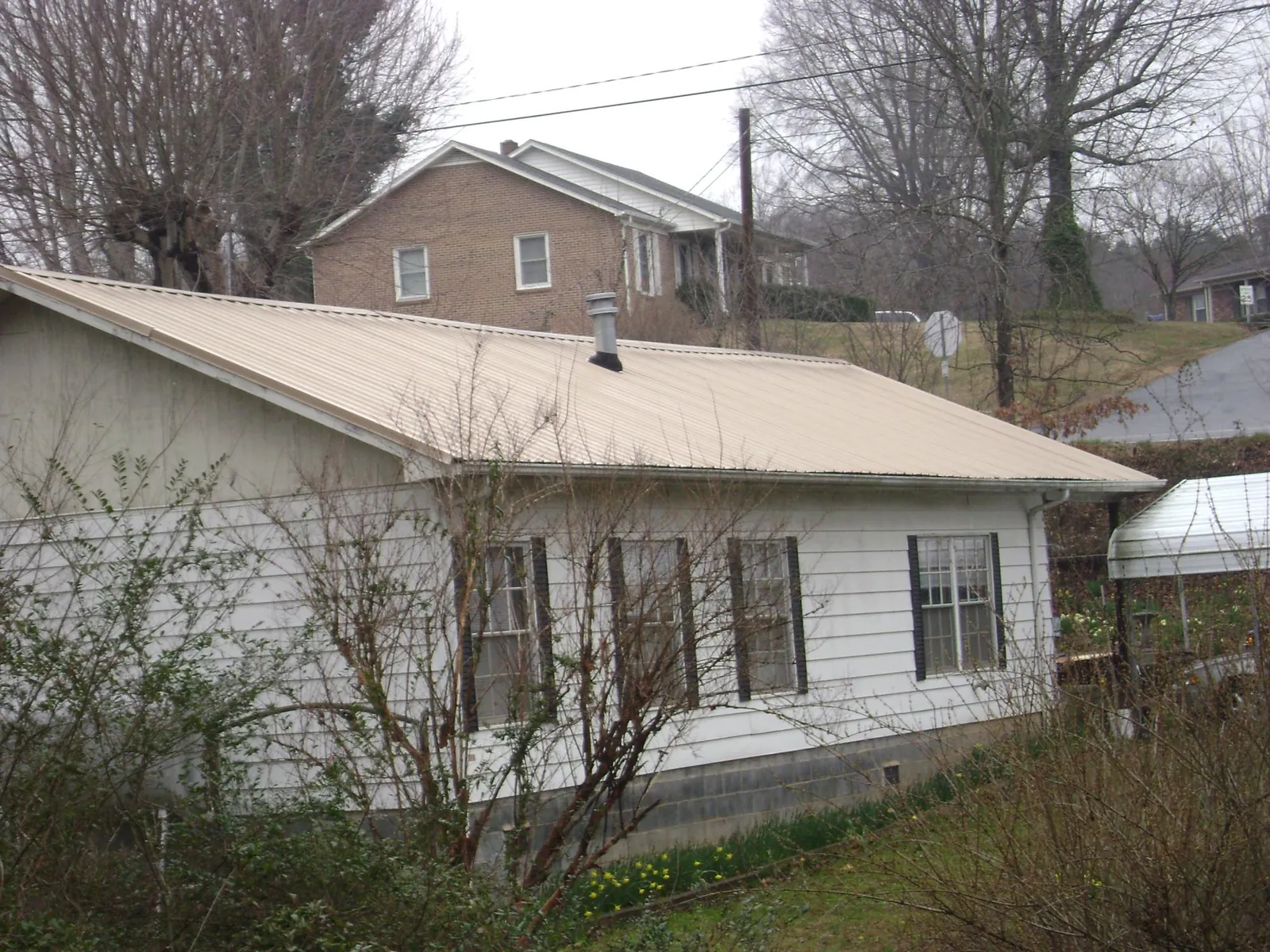 Tan metal roof on a white sided house set into a hillside — Commercial Roofing by Roofing Brothers in Lakebay